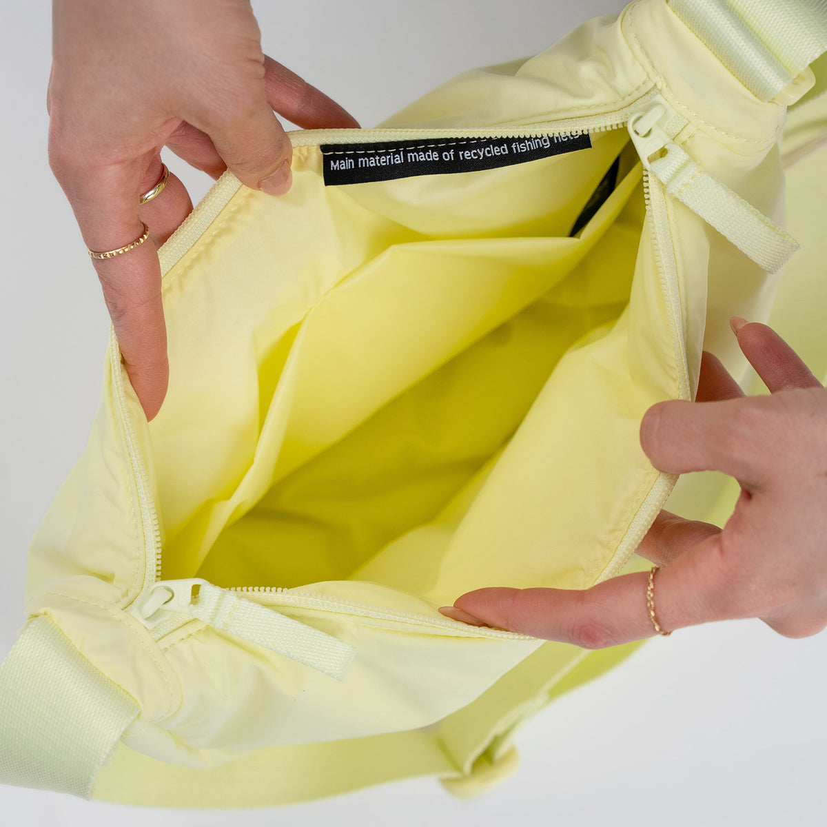 CLOUD MOON BAG SMALL Tasche in sea lemon (zartes Pastellgelb), Innenansicht von Händen geöffnet mit Materialetikett.