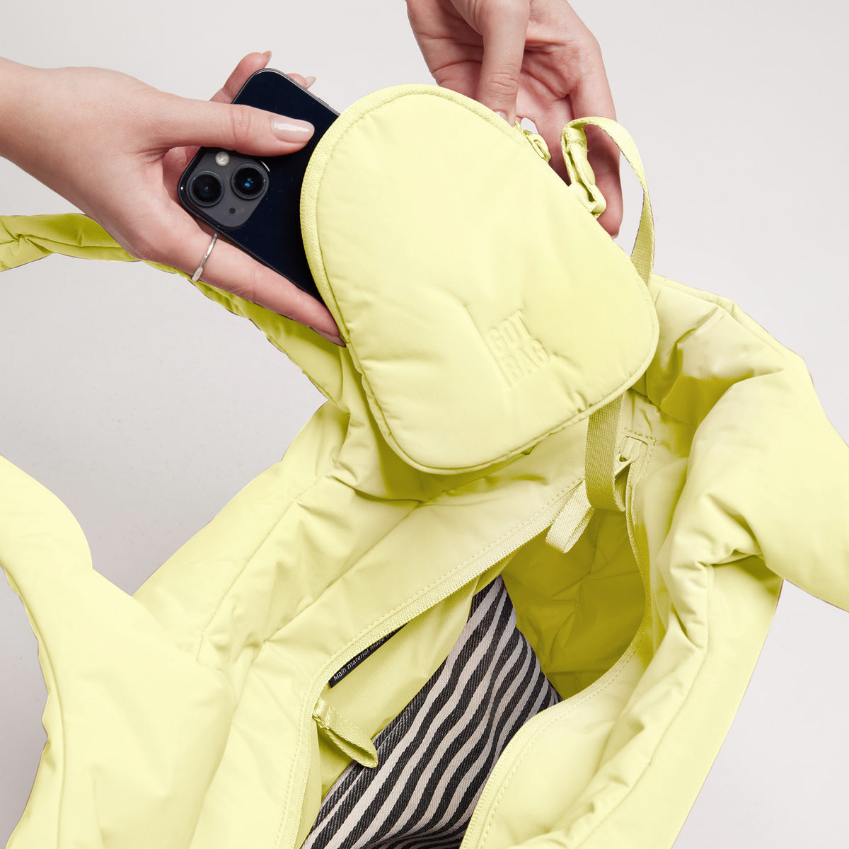 CLOUD TOTE BAG Tasche in sea lemon (zartes Pastellgelb), eine Frau steckt ein Handy in die Pouch.