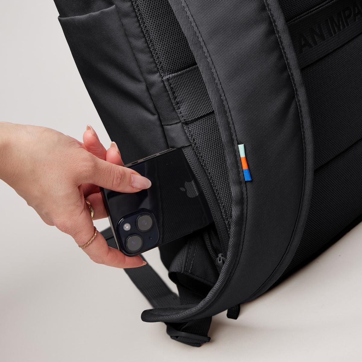 BARREL PACK Rucksack in black (Schwarz), eine Frau steckt Handy in die Seitentasche.