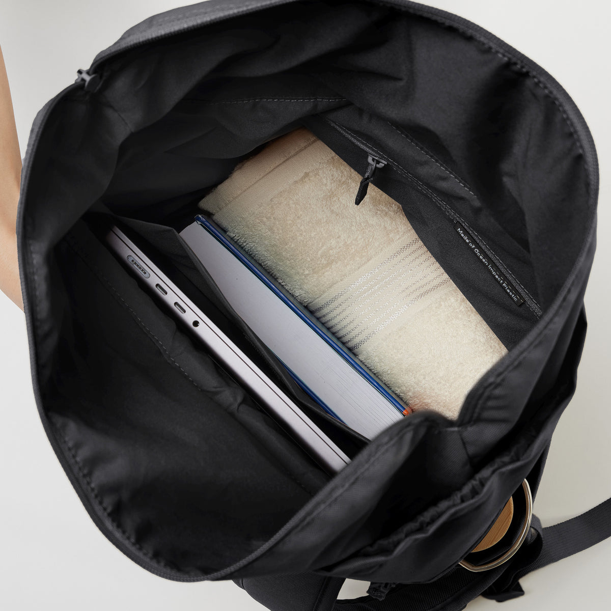 BARREL PACK Rucksack in black (Schwarz) mit Blick ins Innere, gefüllt mit Laptop, Buch und Handtuch.