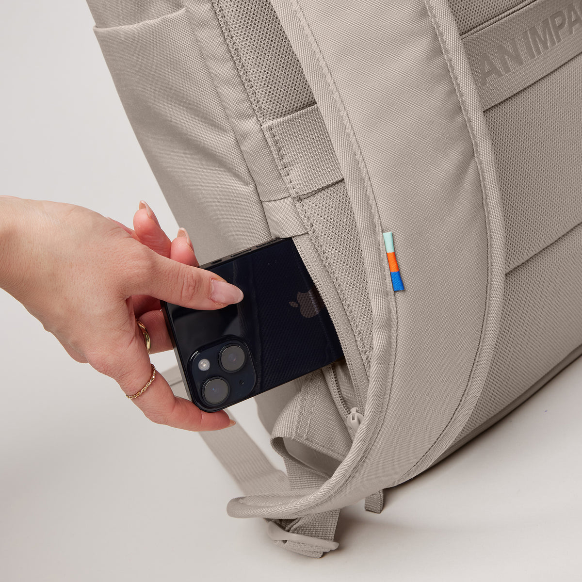 BARREL PACK Rucksack in scallop (helles Beige), eine Frau steckt ein Smartphone in die Seitentasche.