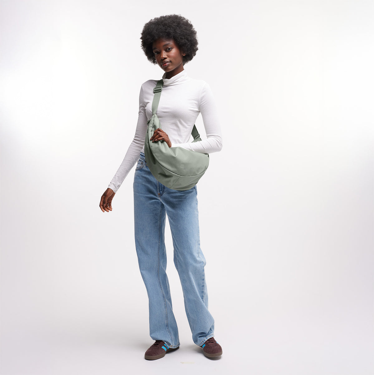 MOON BAG LARGE Tasche in bass (Salbeigrün) von einer Frau crossbody getragen.