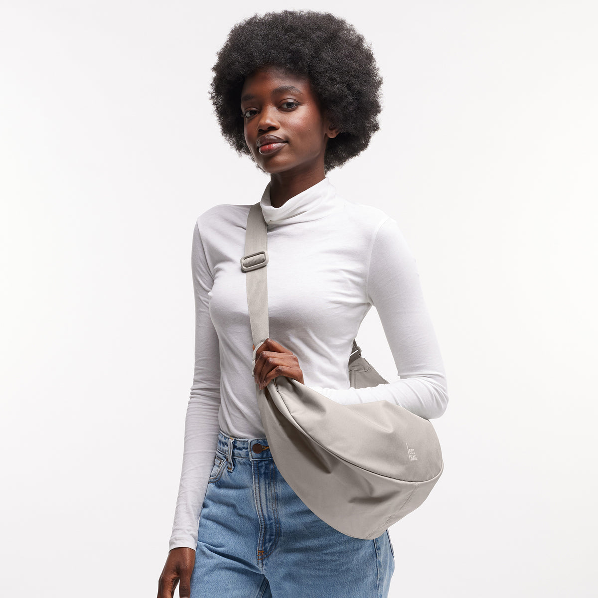 MOON BAG LARGE Tasche in clam (helles, warmes Grau) von einer Frau über der Schulter getragen.