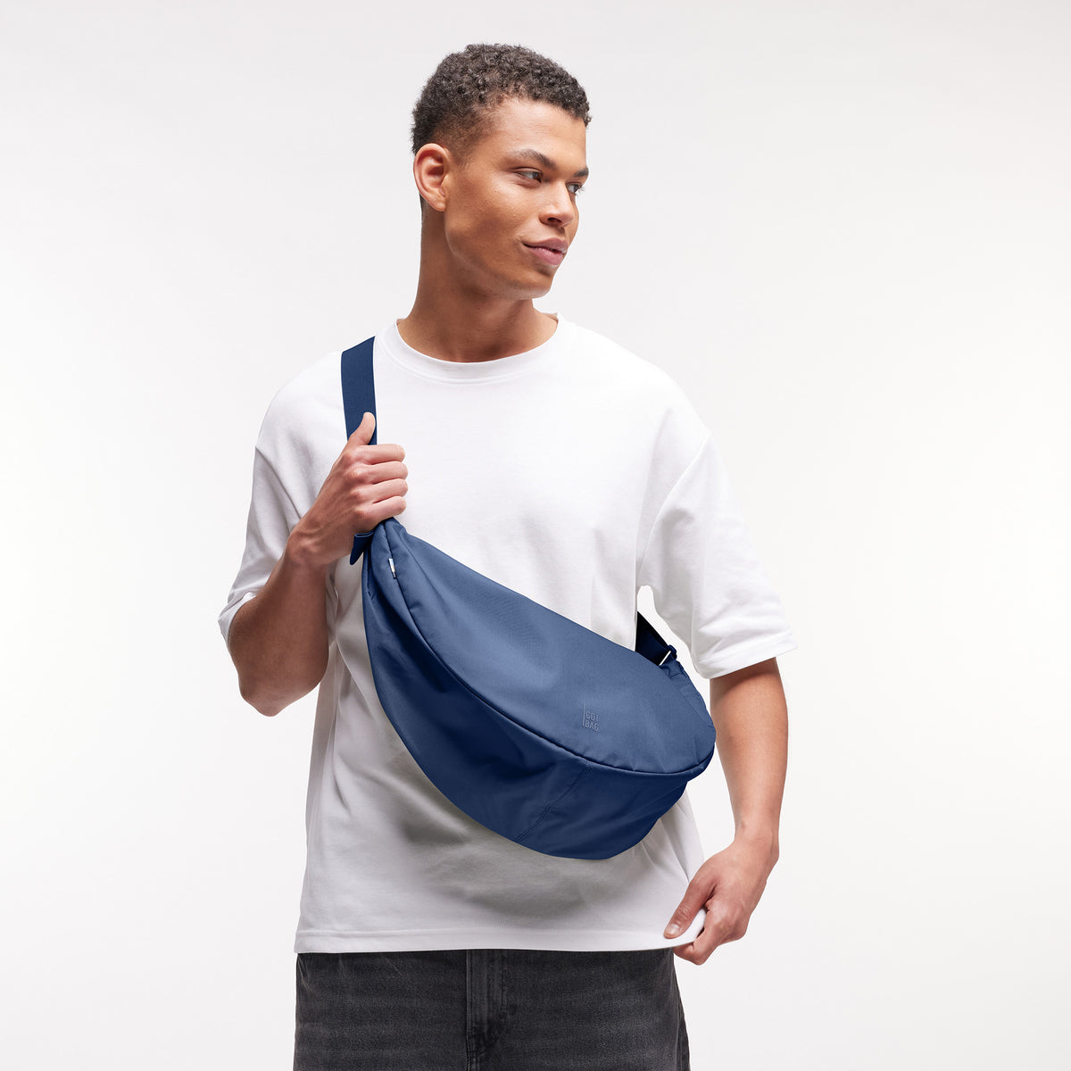 MOON BAG LARGE Tasche in deep ocean (dunkles Marineblau) von einem Mann crossbody getragen.