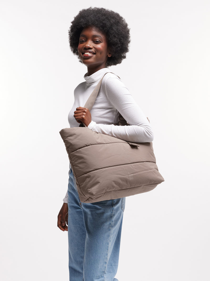 PUFFER TOTE BAG Tasche in oyster (klassisches Taupe-Braun) von einer Frau über der Schulter getragen.