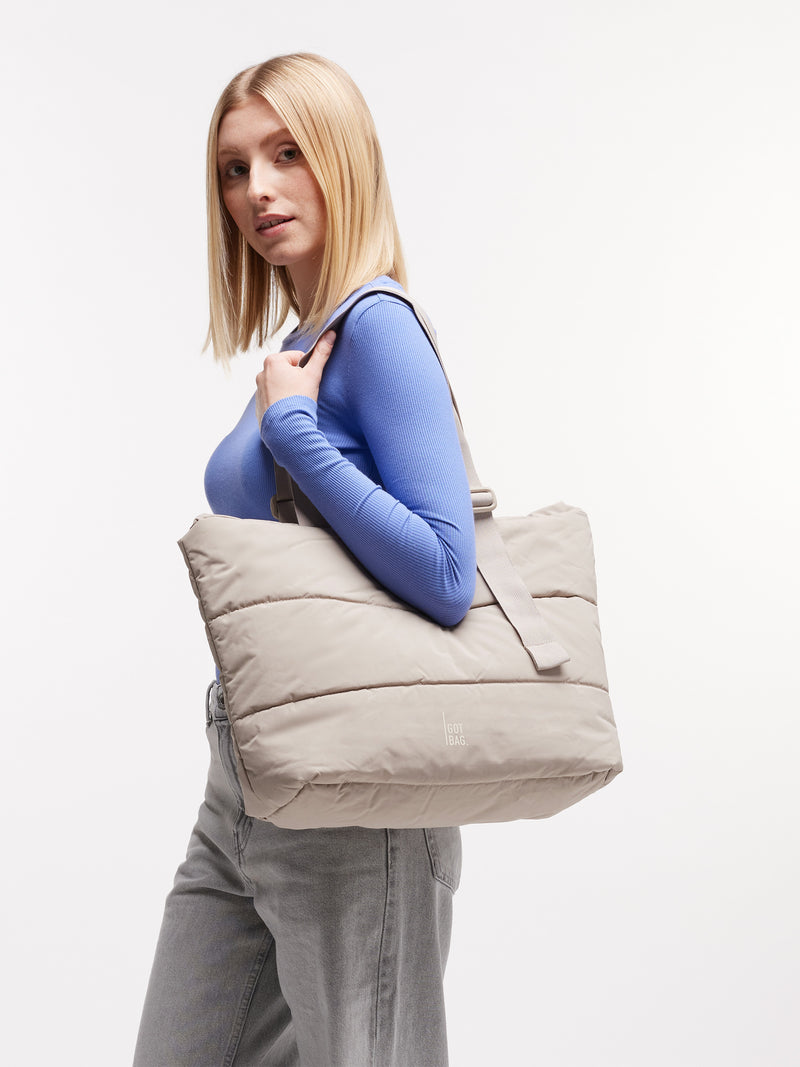 PUFFER TOTE BAG Tasche in scallop (helles Beige) von einer Frau über der Schulter getragen.
