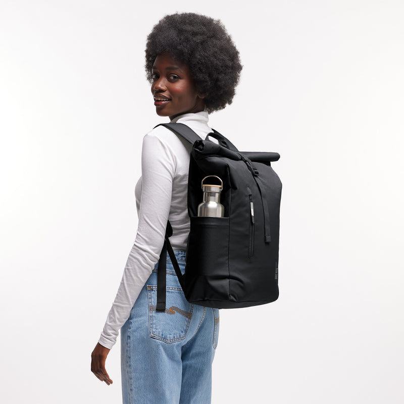 ROLLTOP EASY Rucksack in black (Schwarz), von einer Frau auf dem Rücken getragen, mit Wasserflasche in Seitentasche.