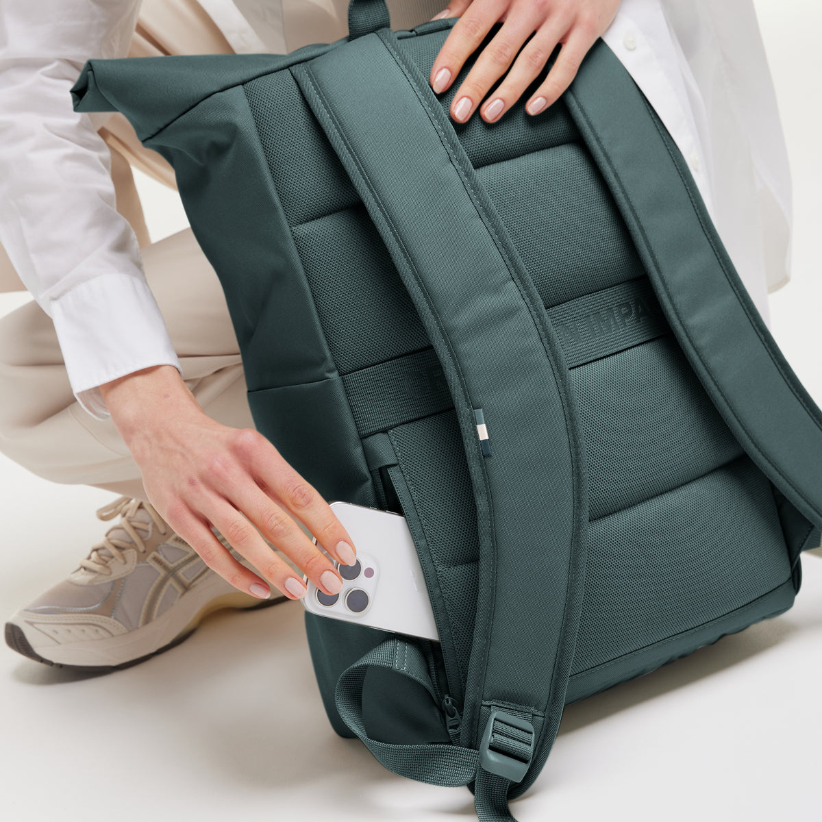 ROLLTOP EASY Monochrome Edition Rucksack in sea teal (kühles Türkisgrün) von einer Frau, die ein Smartphone in die Seitentasche steckt.