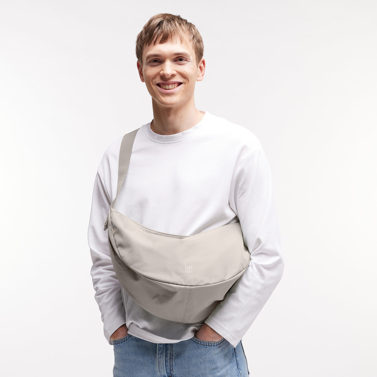 MOON BAG LARGE Tasche in clam (helles, warmes Grau) von einem Mann crossbody getragen.