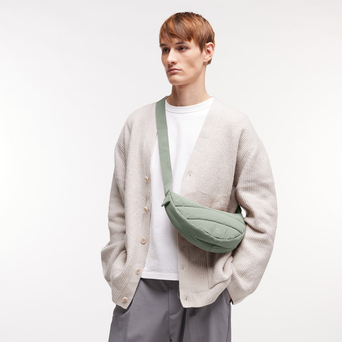 PUFFER MOON BAG SMALL Tasche in bass (Salbeigrün) von einem Mann crossbody getragen.