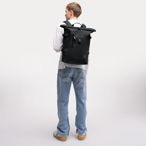 ROLLTOP Rucksack in black (Schwarz) von einem Mann auf dem Rücken getragen.