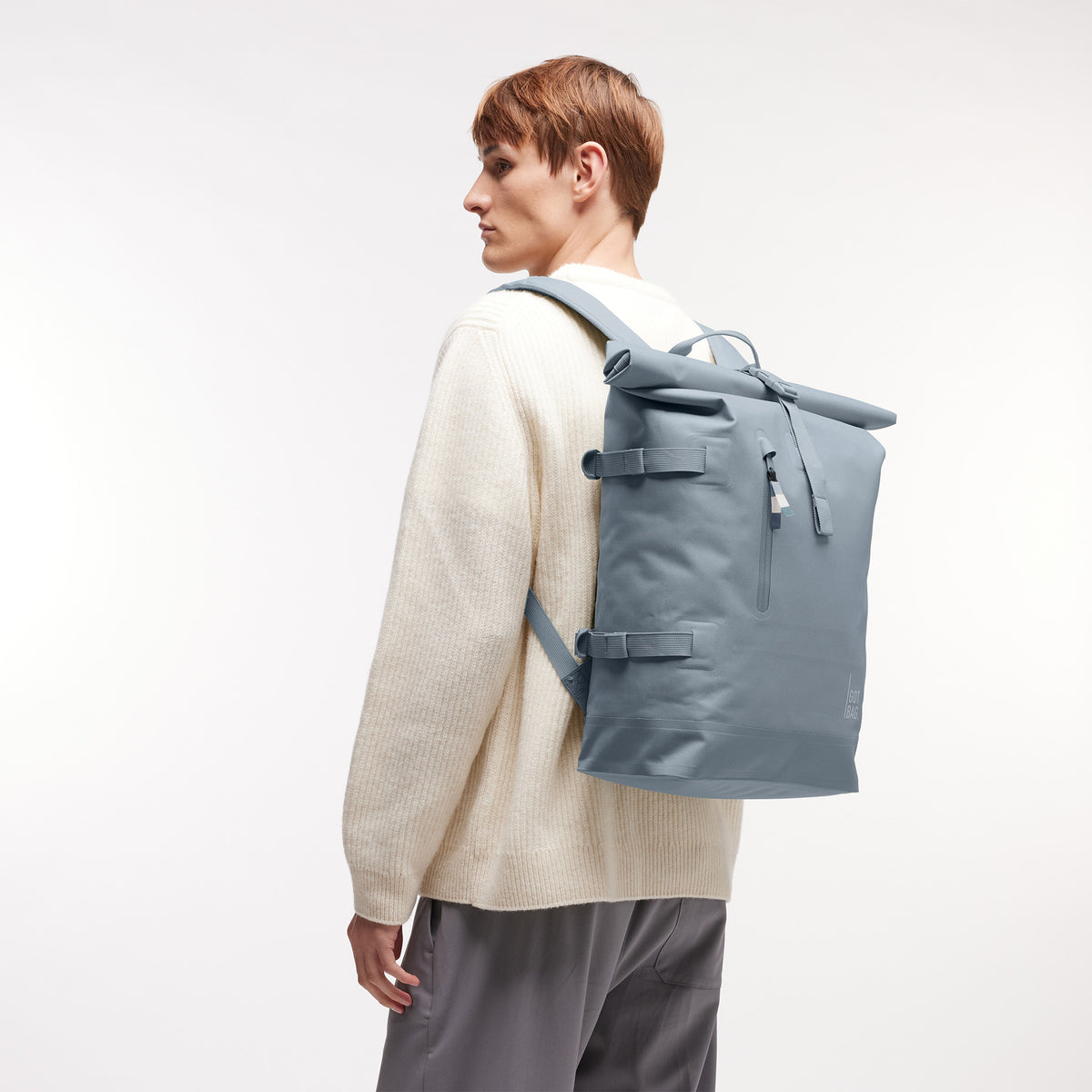 ROLLTOP MONOCHROME EDITION Rucksack in marlin (grau-blau) von einem Mann auf dem Rücken getragen.