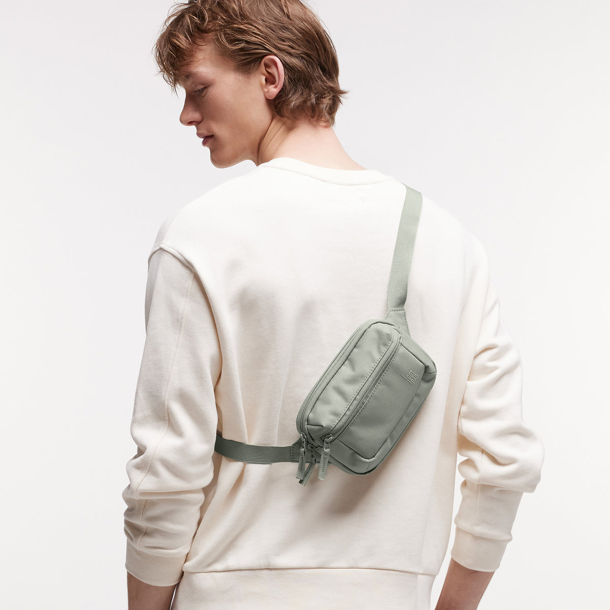 SLING BAG SMALL Tasche in bass (Salbeigrün) von einem Mann crossbody getragen.