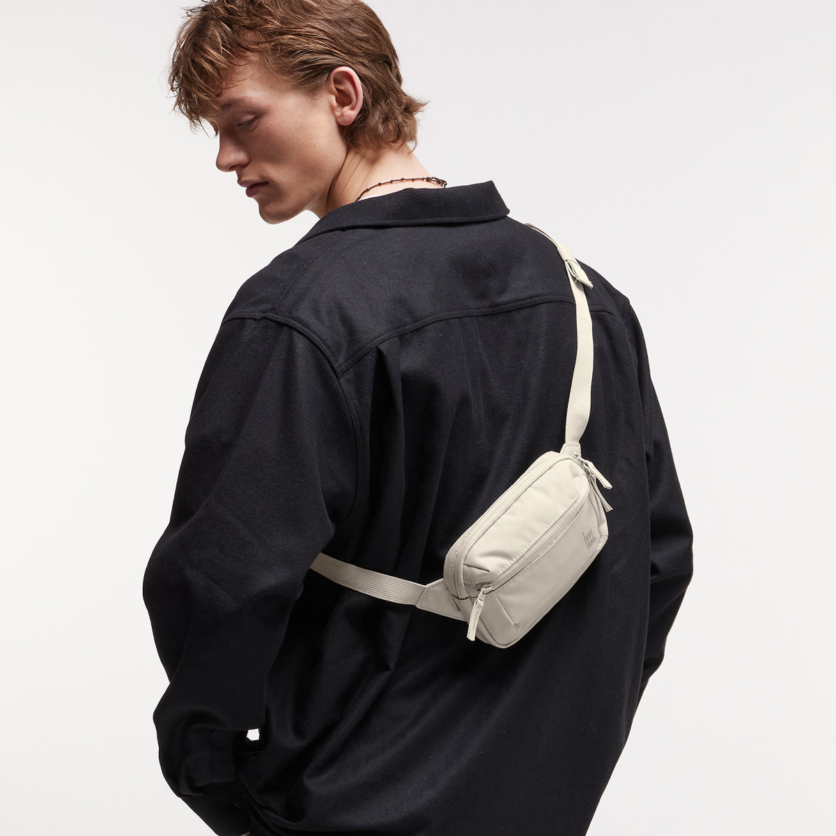 SLING BAG SMALL Tasche in soft shell (warmes Cremeweiß) von einem Mann crossbody getragen.