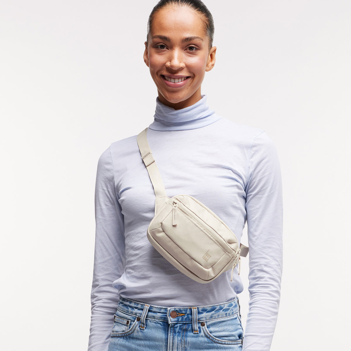 SLING BAG SMALL Tasche in soft shell (warmes Cremeweiß) von einer Frau crossbody getragen.