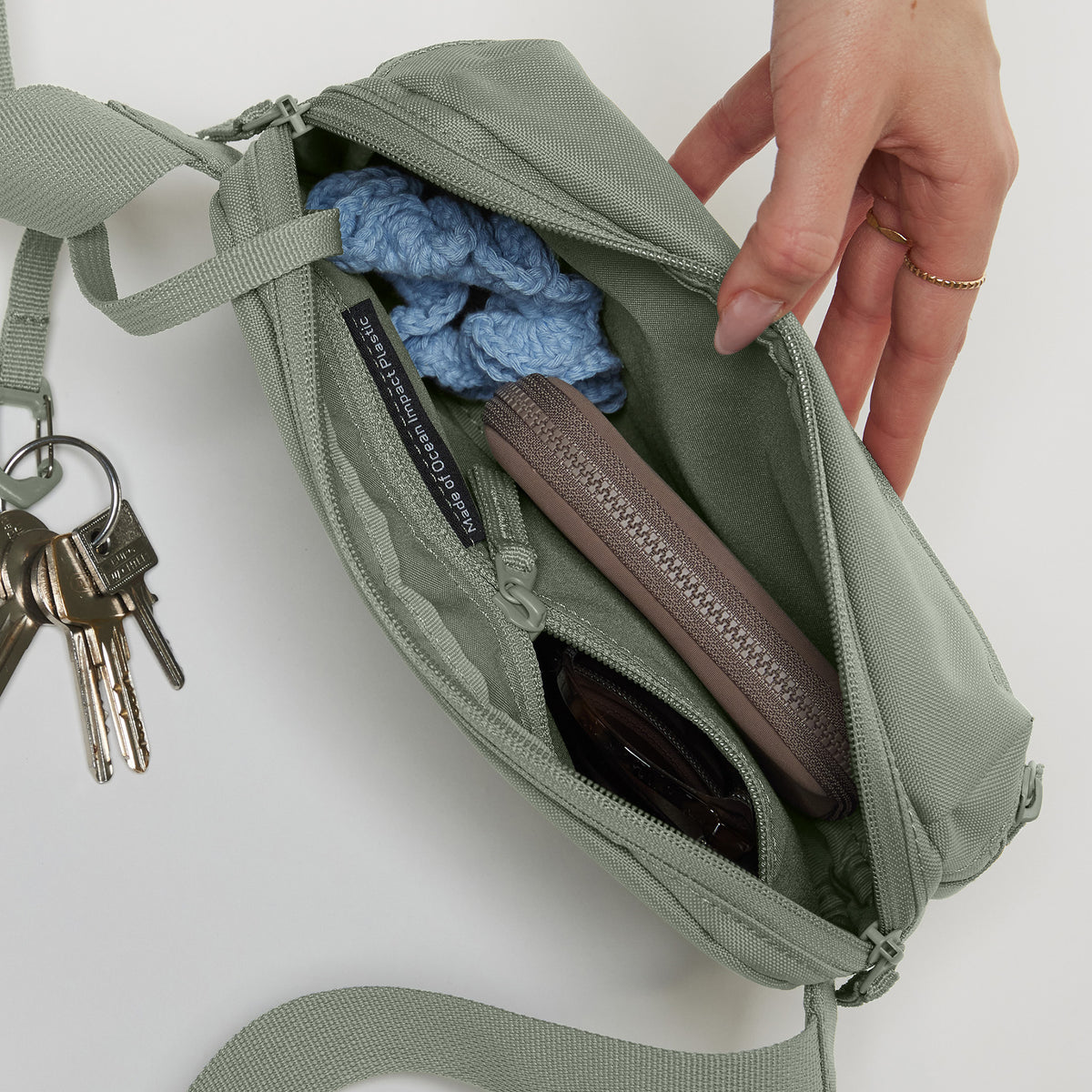 SLING BAG Tasche in bass (Salbeigrün) von einer Frau geöffnet.