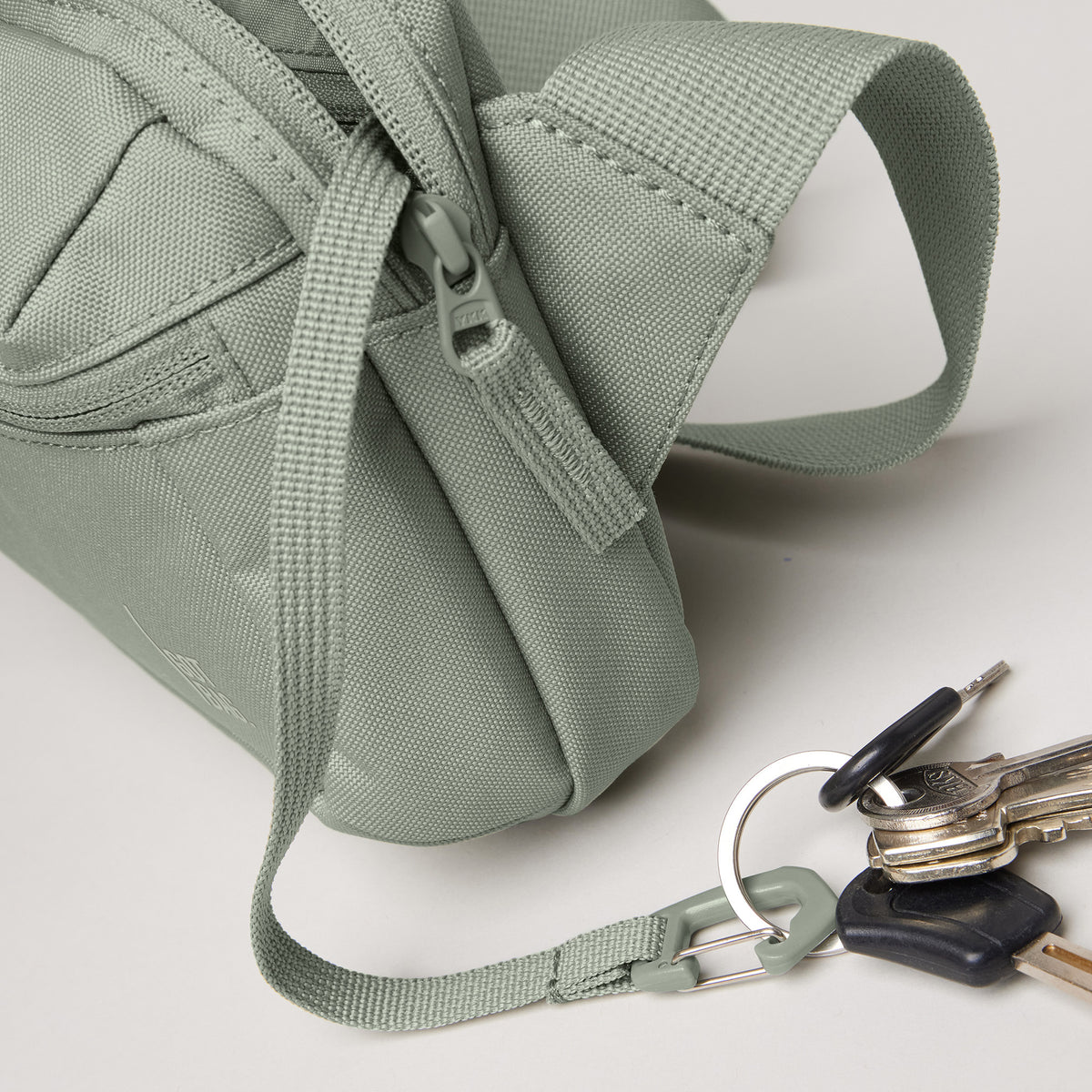 SLING BAG Tasche in bass (Salbeigrün) auf hellem Untergrund mit Schlüsseln daneben.
