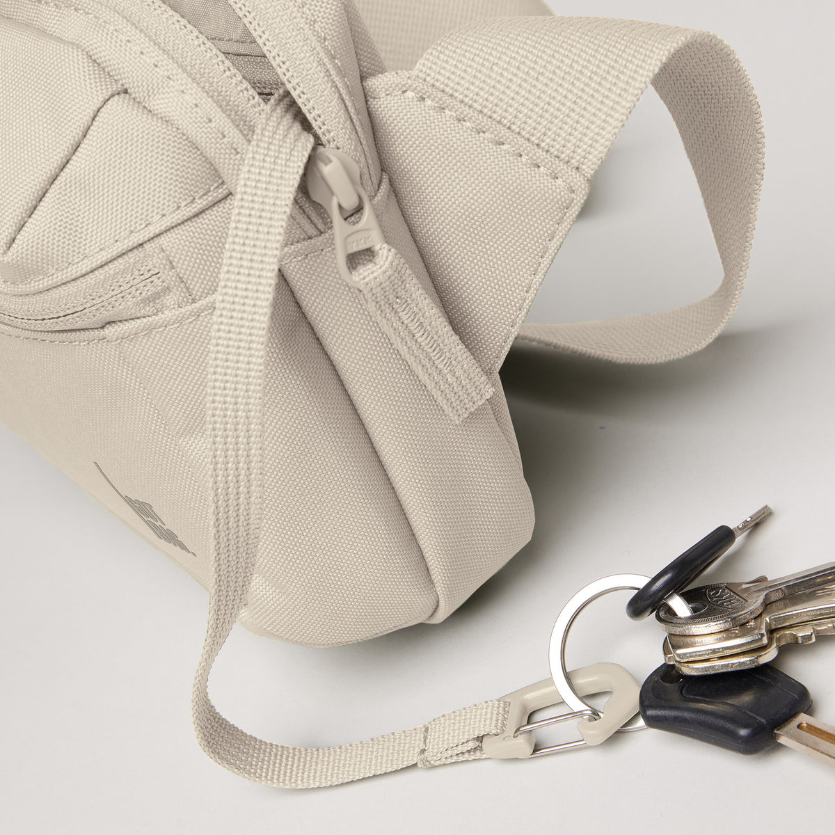 SLING BAG Tasche in soft shell (warmes Cremeweiß) mit Schlüsseln am Tragegurt liegend.