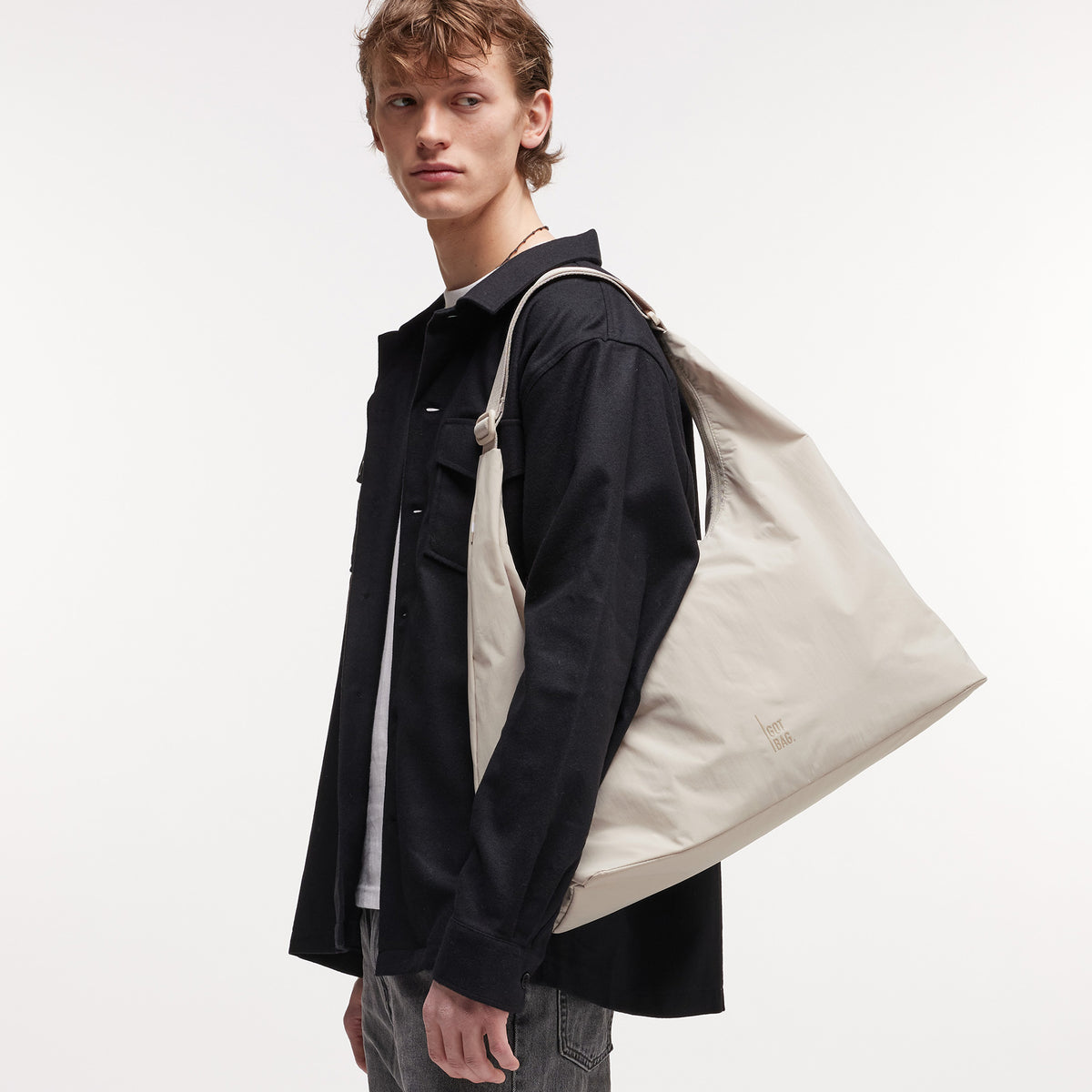 T SHAPE BAG LARGE Tasche in soft shell (warmes Cremeweiß) von einem Mann über der Schulter getragen.