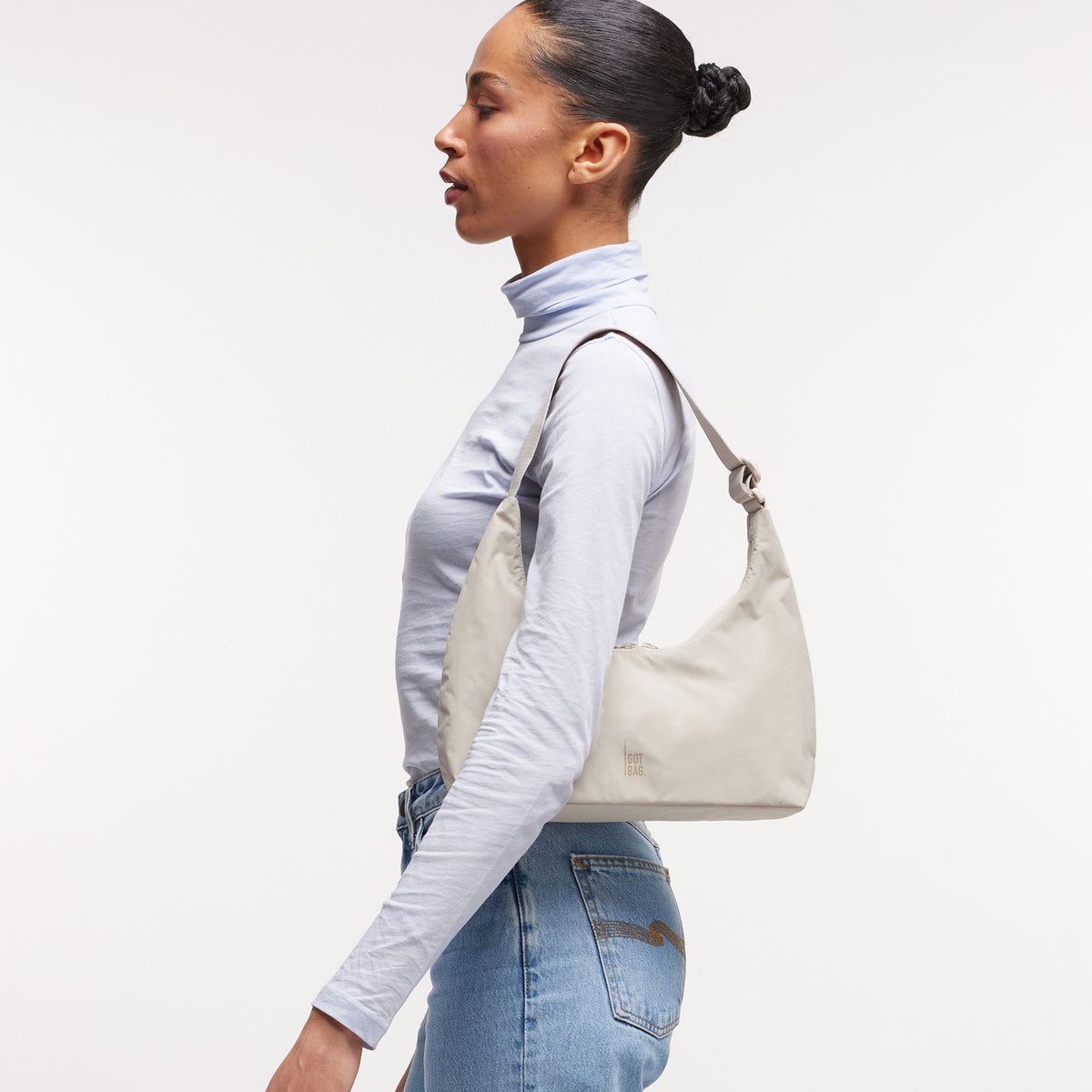 T SHAPE BAG MINI Tasche in soft shell (warmes Cremeweiß) von einer Frau über der Schulter getragen.