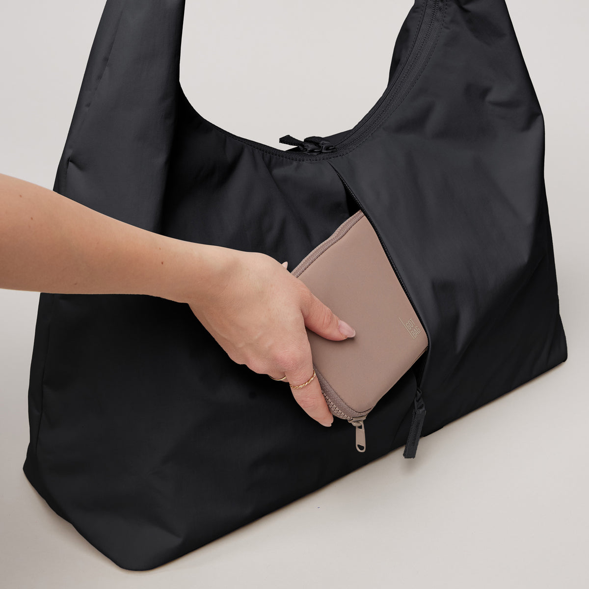 T SHAPE BAG Tasche in black (Schwarz), in die eine Frau eine Brieftasche steckt.