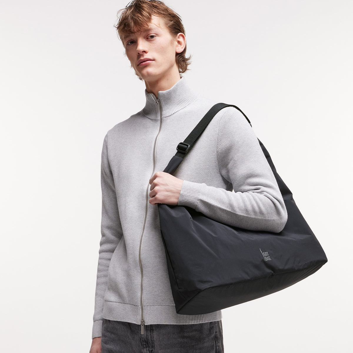 T SHAPE BAG Tasche in black (Schwarz) von einem Mann über der Schulter getragen.