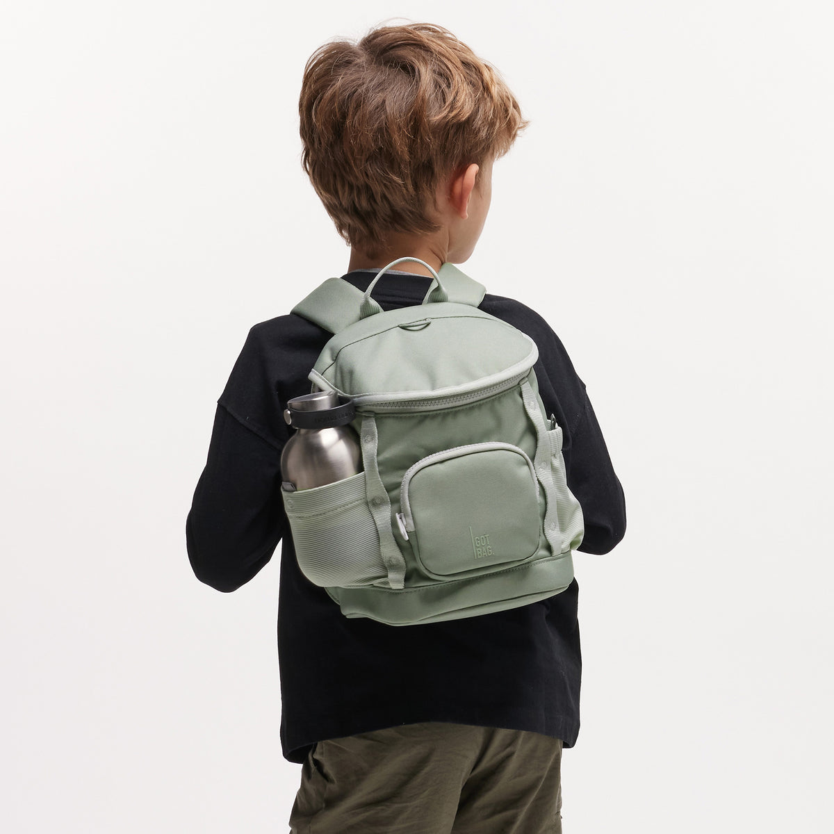 KIDS ADVENTURE DAYPACK Rucksack in bass (Salbeigrün) von einem Kind auf dem Rücken getragen.