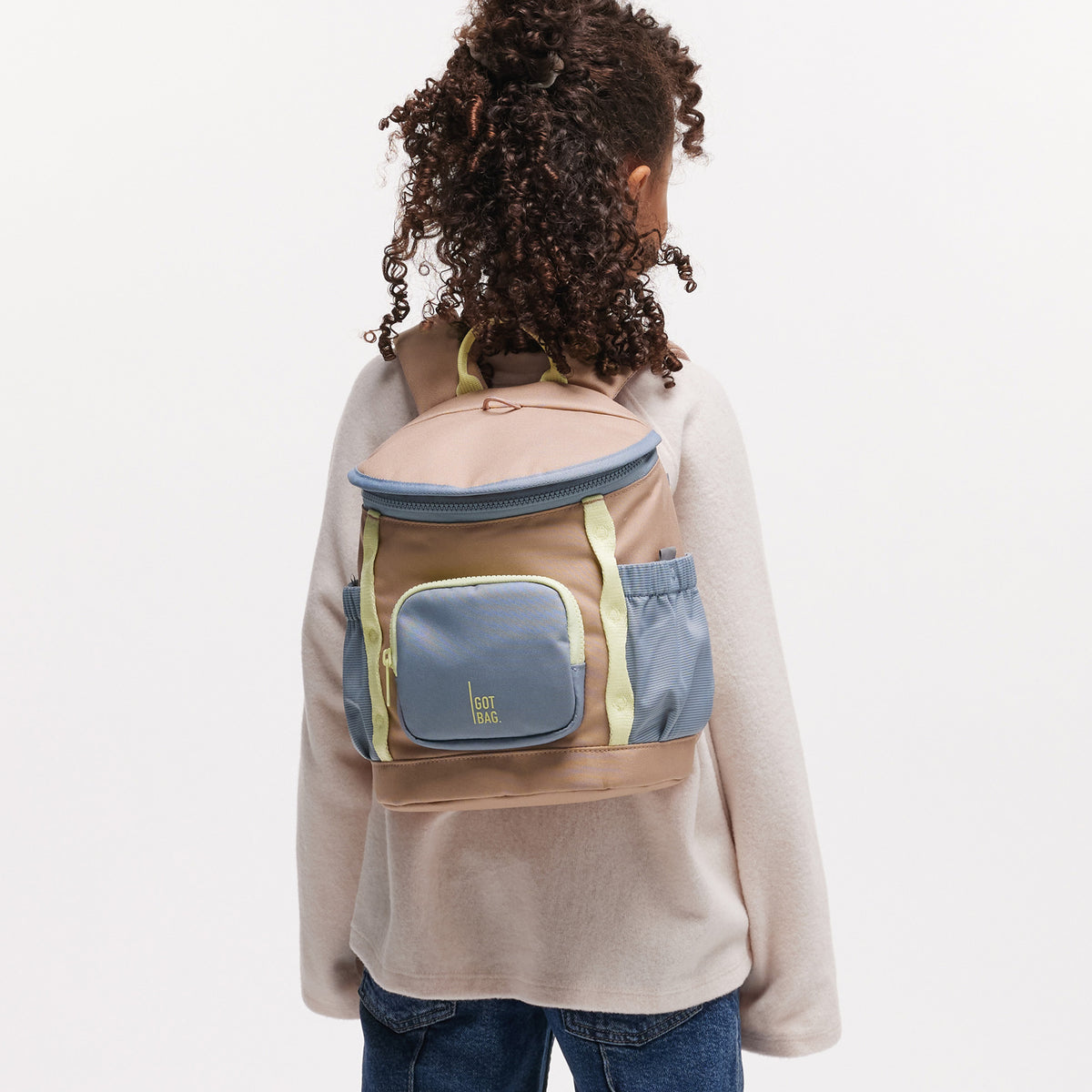 KIDS ADVENTURE DAYPACK Rucksack in sandbar (warmes Beige mit rötlichem Unterton) von einer Person auf dem Rücken getragen.