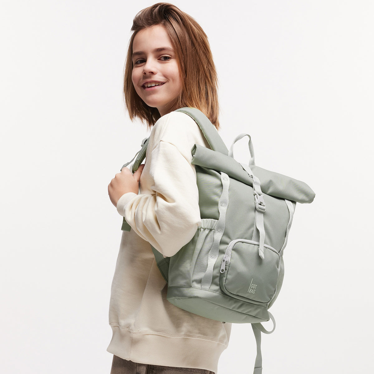 KIDS ADVENTURE ROLLTOP Rucksack in bass (Salbeigrün) von einem Mädchen als Rucksack auf dem Rücken getragen.