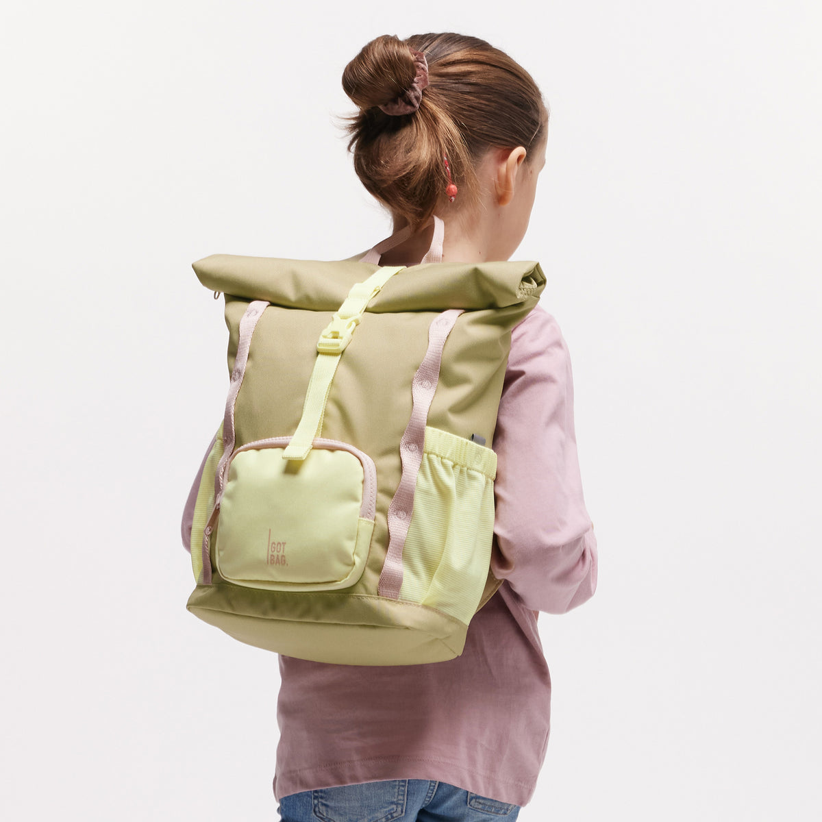 KIDS ADVENTURE ROLLTOP Rucksack in nori (pastellfarbenes Pistaziengrün) von einem Mädchen auf dem Rücken getragen.