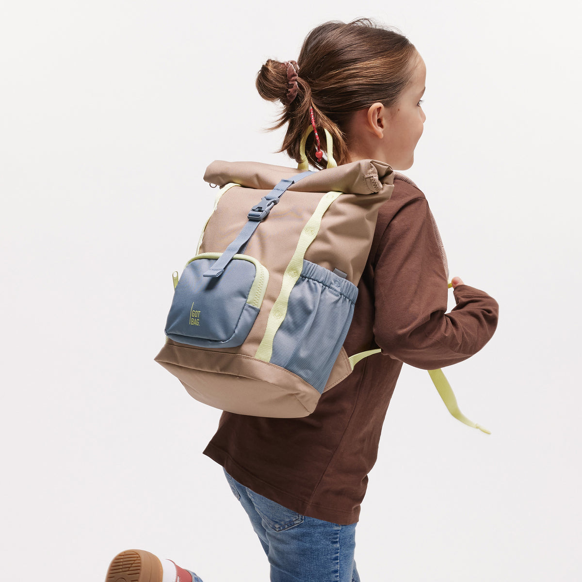 KIDS ADVENTURE ROLLTOP Rucksack in sandbar (warmes Beige mit rötlichem Unterton) von einem Mädchen auf dem Rücken getragen.