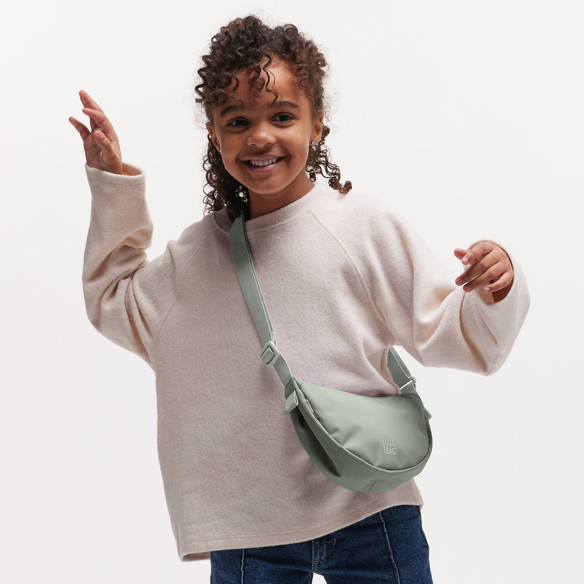 MOON BAG MINI Tasche in bass (Salbeigrün) von einer Person crossbody getragen.