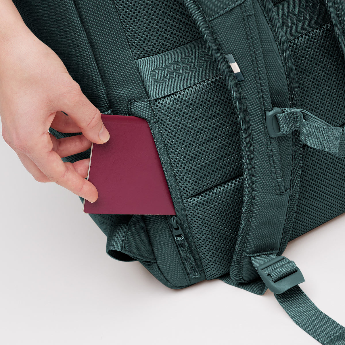 PRO PACK Monochrome Edition Rucksack in sea teal (kühles Türkisgrün). Detailaufnahme, wie eine Hand einen Reisepass in eine Tasche steckt.