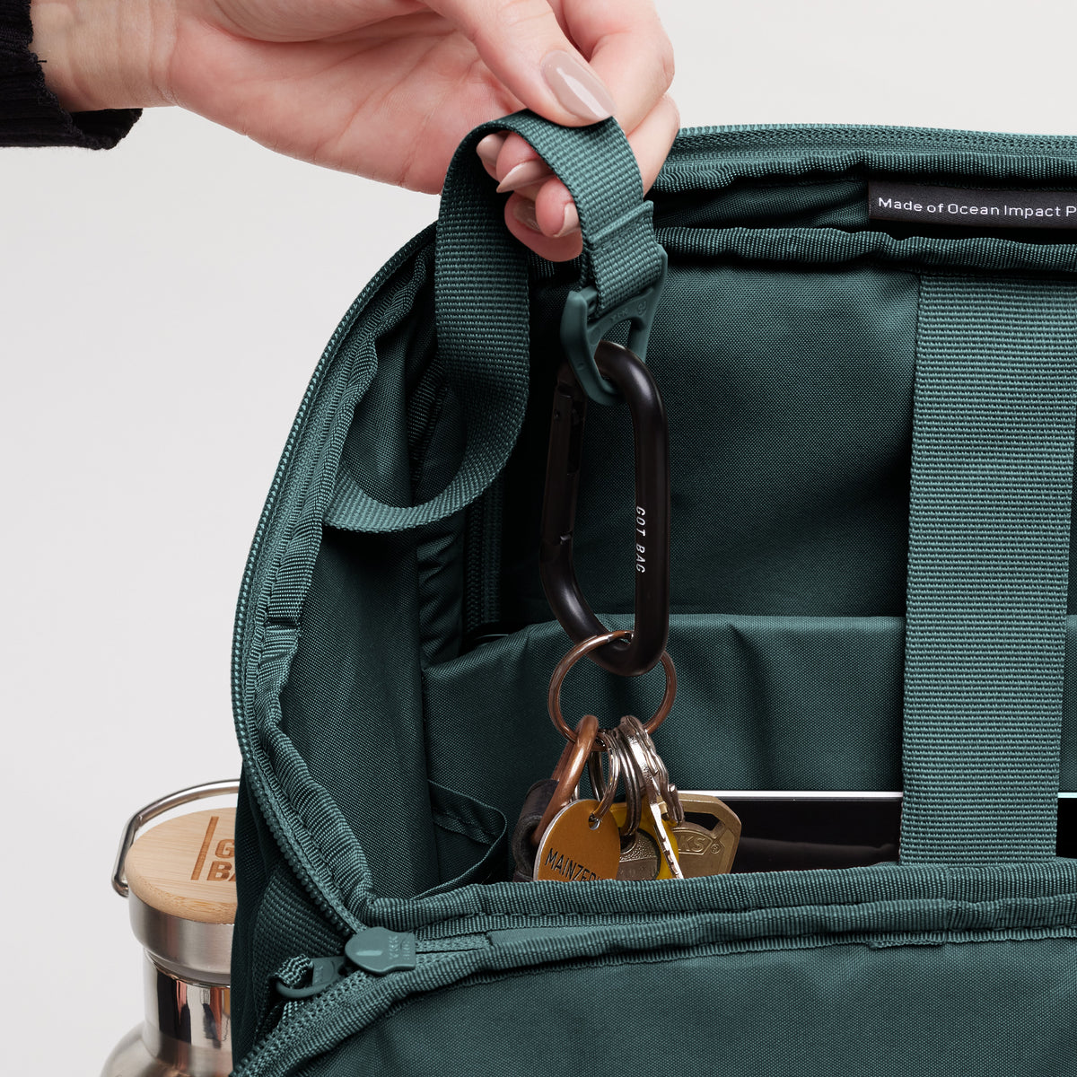 Detailaufnahme des PRO PACK Rucksacks in sea teal (kühles Türkisgrün), eine Hand hält den Riemen, Schlüssel am Karabiner.