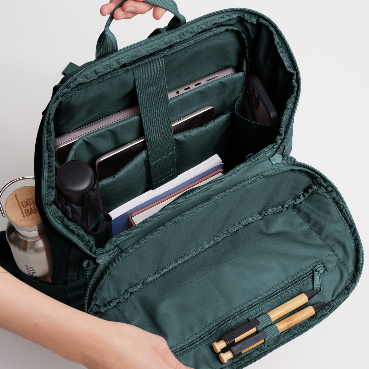 PRO PACK Rucksack in sea teal (kühles Türkisgrün), offen mit Laptop, Flasche und Stiften, von Händen gehalten.