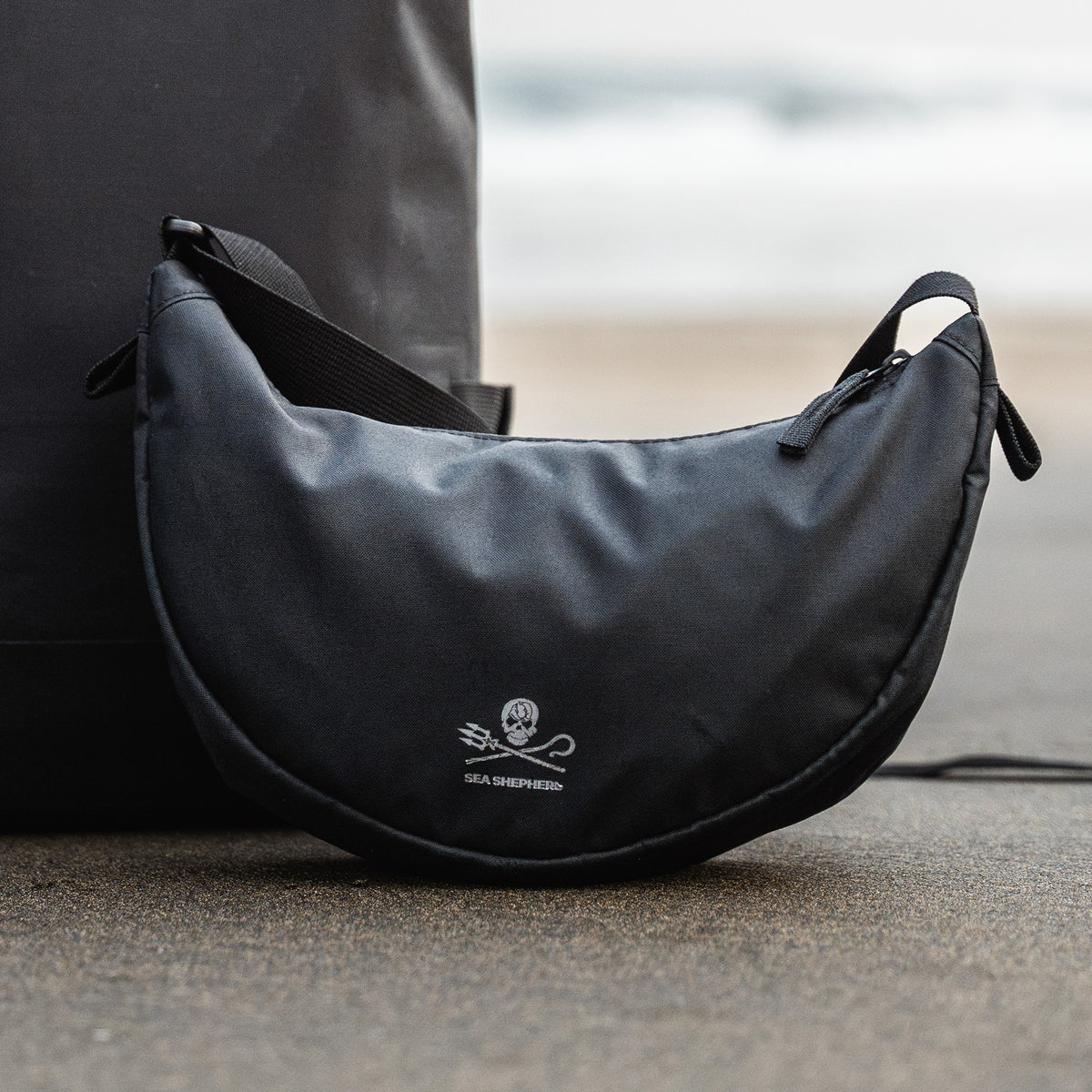 MOON BAG SMALL Tasche in black (Schwarz) auf dem Sand liegend.