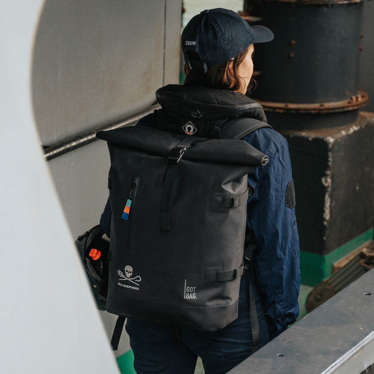 ROLLTOP 2.0 Rucksack in black (Schwarz) von einer Frau auf dem Rücken getragen, mit Sea Shepherd und GOT BAG Logos.