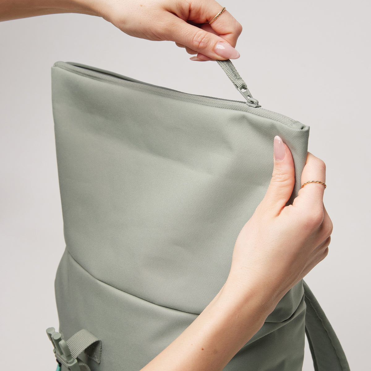 ROLLTOP EASY SMALL Rucksack in bass (Salbeigrün) von einer Frau geöffnet und in den Händen gehalten.