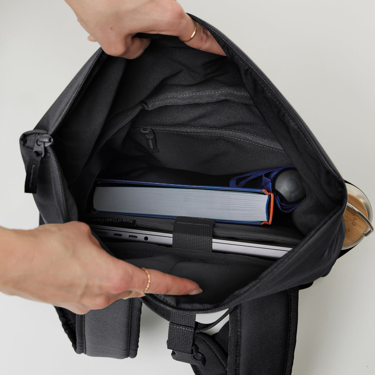 Frau hält ROLLTOP EASY SMALL Rucksack in black (Schwarz) offen, Laptop, Buch und Flasche sichtbar.