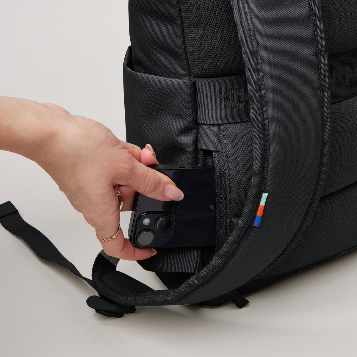 ROLLTOP EASY SMALL Rucksack in black (Schwarz) von einer Frau, die ein Smartphone in die Seitentasche steckt.