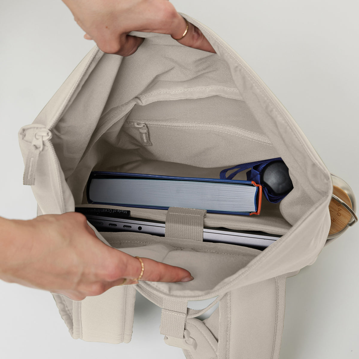ROLLTOP EASY SMALL Rucksack in soft shell (warmes Cremeweiß), von einer Frau geöffnet, zeigt Laptop & Buch.
