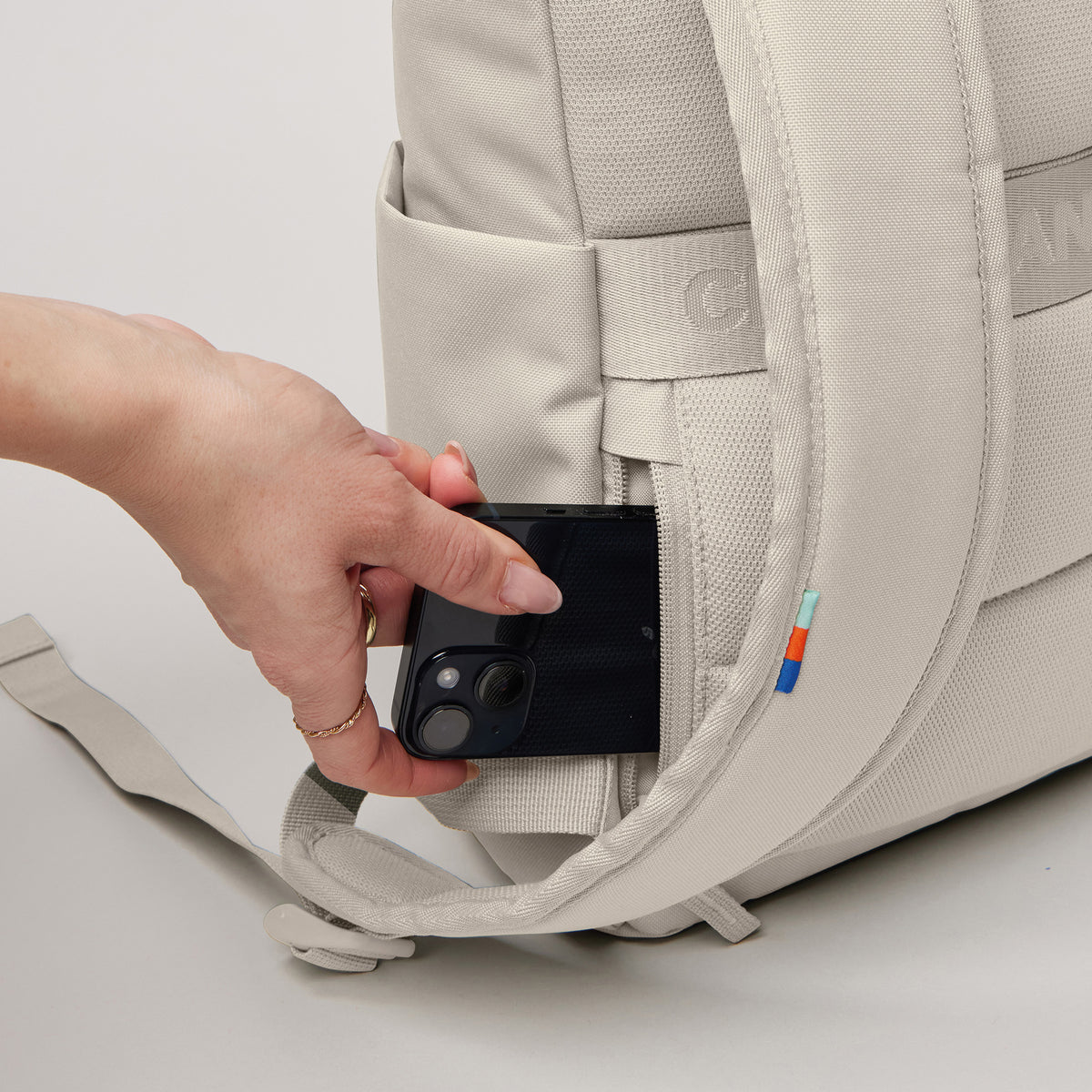 ROLLTOP EASY SMALL Rucksack in soft shell (warmes Cremeweiß) von einer Frau in eine Seitentasche gesteckt.