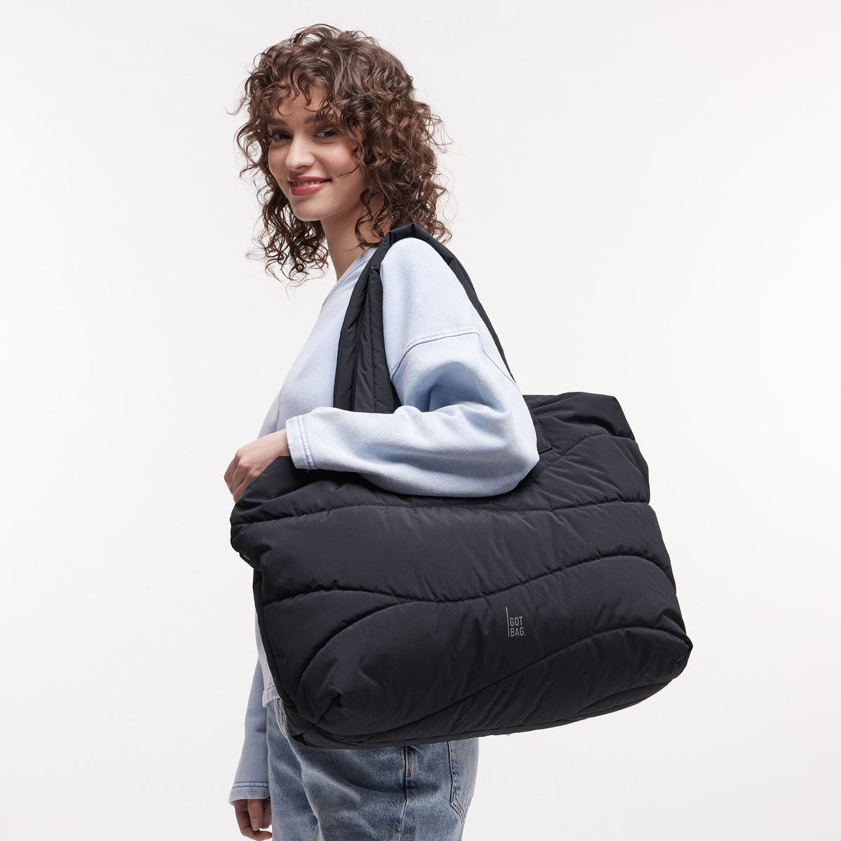 WAVY PUFFER EVERYDAY BAG Tasche in black (Schwarz) von einer Frau über der Schulter getragen.