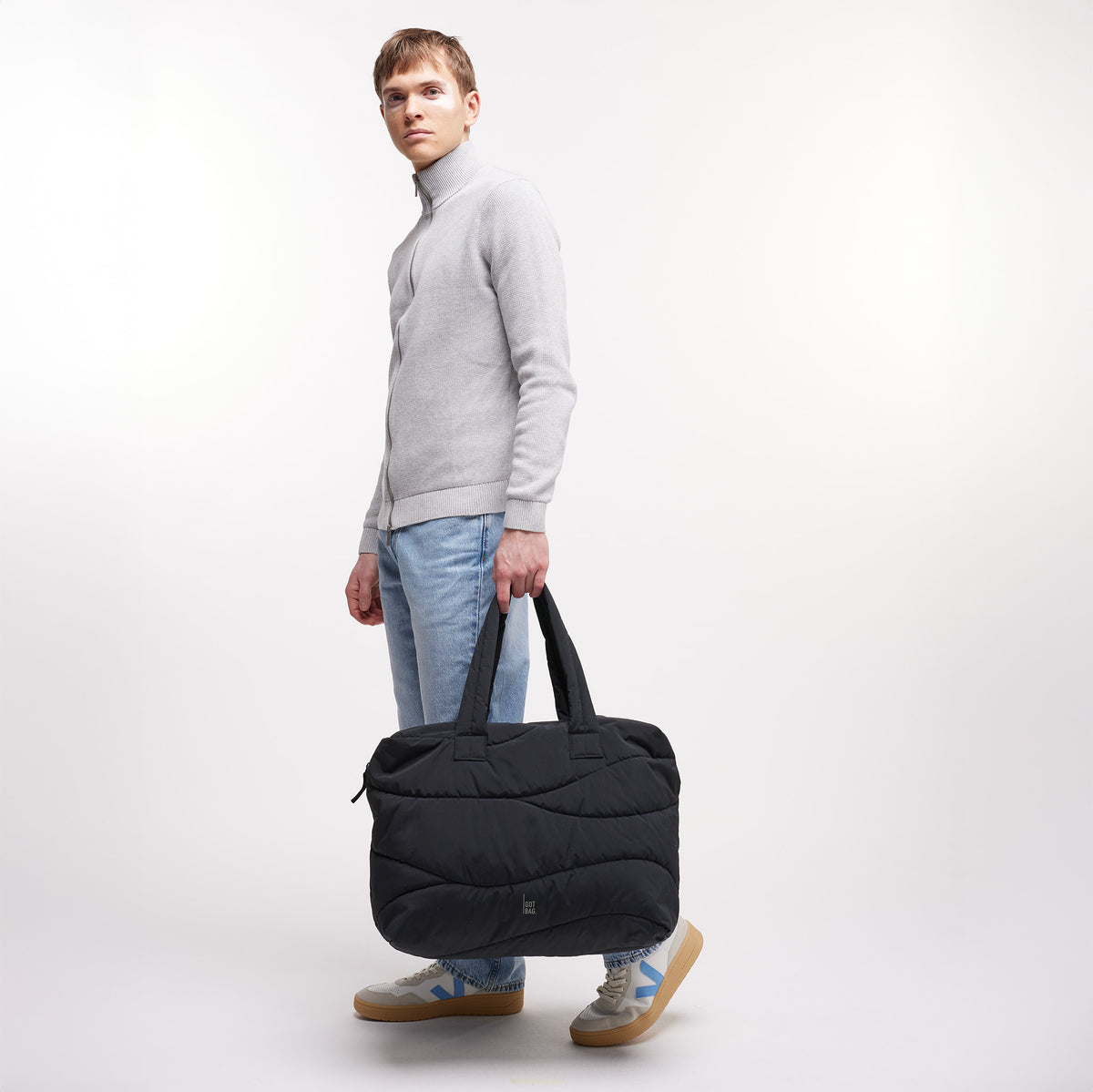 WAVY PUFFER EVERYDAY BAG Tasche in black (Schwarz) von einem Mann in der Hand gehalten.