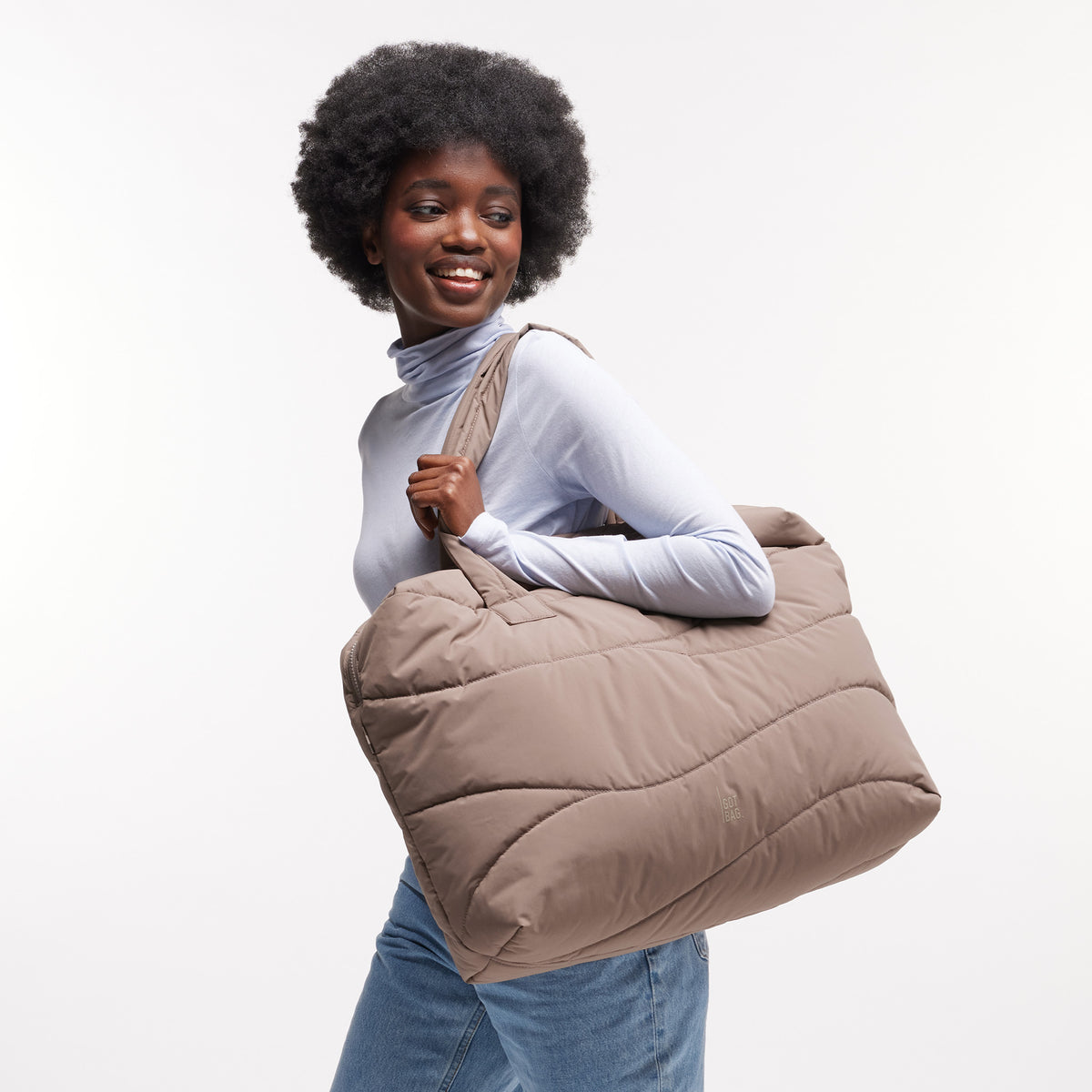 WAVY PUFFER EVERYDAY BAG Tasche in oyster (klassisches Taupe-Braun) von einer Frau über der Schulter getragen.
