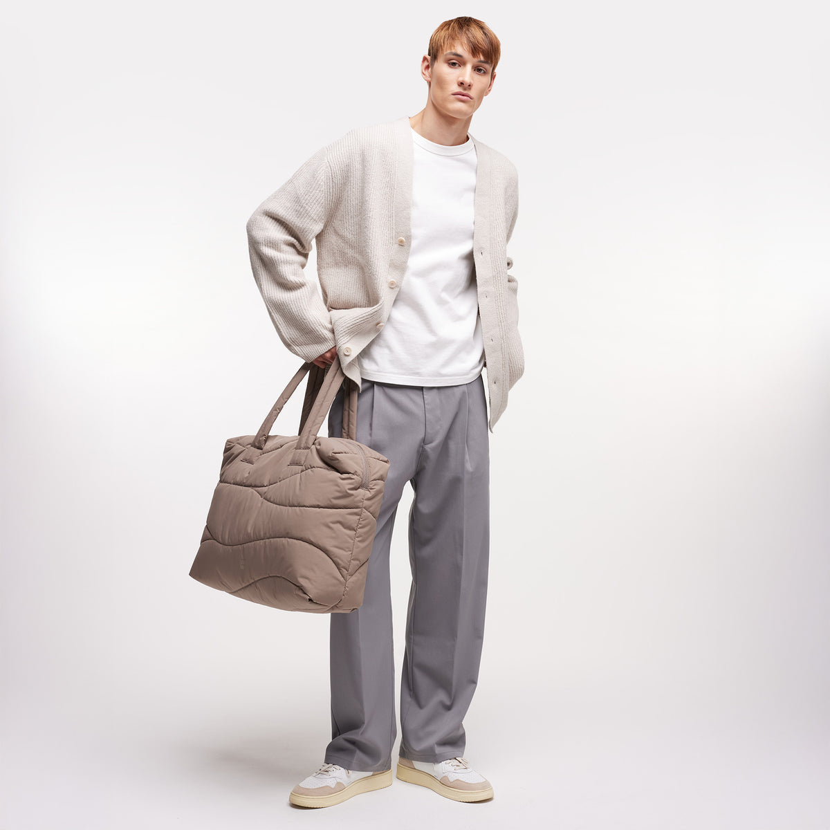 WAVY PUFFER EVERYDAY BAG Tasche in oyster (klassisches Taupe-Braun) von einem Mann in der Hand gehalten.