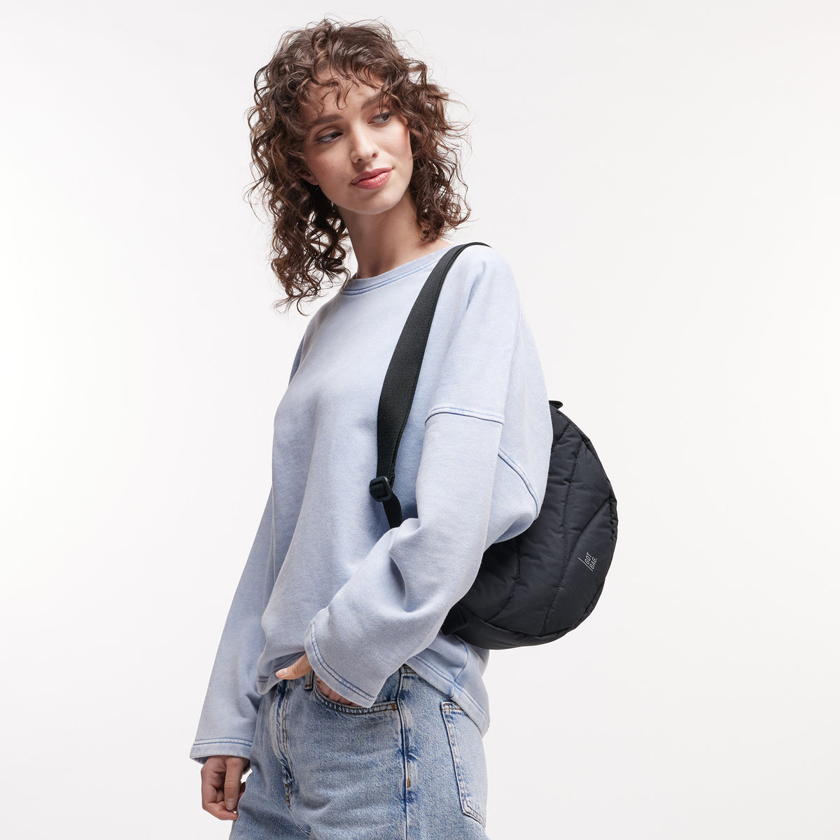 WAVY PUFFER MOON BAG Tasche in black (Schwarz) von einer Frau über der Schulter getragen.