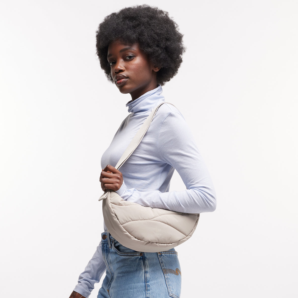 WAVY PUFFER MOON BAG Tasche in scallop (helles Beige) von einer Frau crossbody getragen.