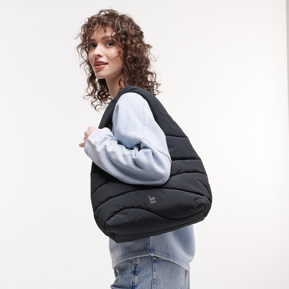 WAVY PUFFER SHOULDER BAG Tasche in black (Schwarz) von einer Frau über der Schulter getragen.