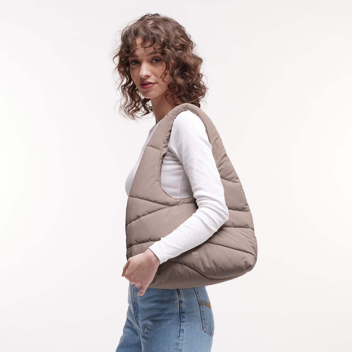 WAVY PUFFER SHOULDER BAG Tasche in oyster (klassisches Taupe-Braun) von einer Frau über der Schulter getragen.